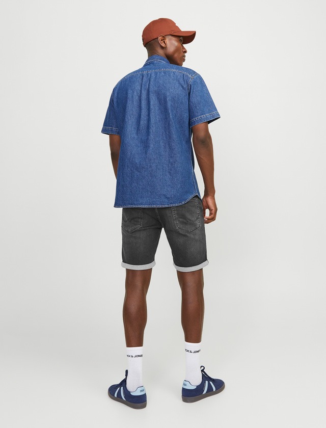Mann von hinten, trägt ein denim Hemd, dunkle Shorts und Sneakers.
