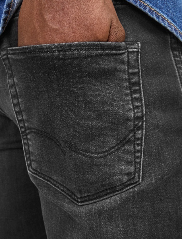 Ein Hand, die in die Gesäßtasche einer dunklen Jeans gesteckt ist.