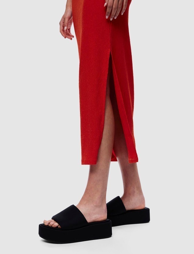 Eine Person trägt ein rotes Kleid mit einem Seitenaufschlag und schwarze Blocksandalen.