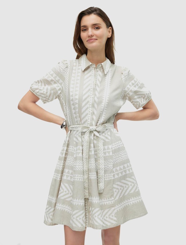 Eine Frau trägt ein helles, gemustertes Kleid mit kurzen Ärmeln und einem Gürtel in der Taille.