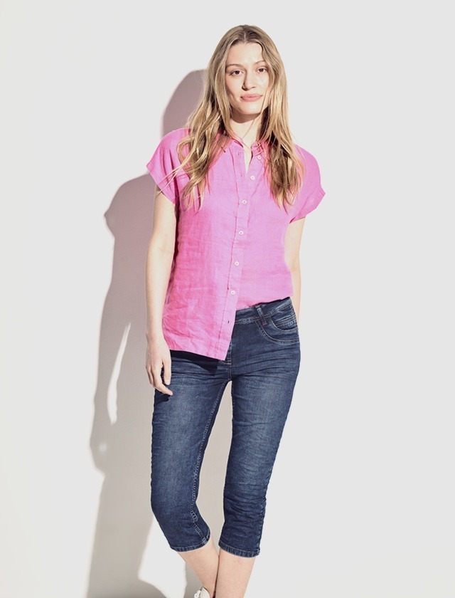 Eine Frau trägt ein pinkes Hemd und Jeans. Sie steht vor einem hellen Hintergrund. Eine Frau trägt ein pinkes Hemd und Jeans. Sie steht vor einem hellen Hintergrund.