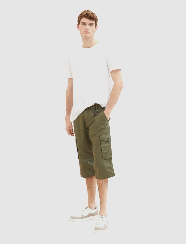 Ein Mann trägt ein weißes T-Shirt und grüne Cargo-Shorts. Er steht in einer neutralen Umgebung. Ein Mann trägt ein weißes T-Shirt und grüne Cargo-Shorts. Er steht in einer neutralen Umgebung.