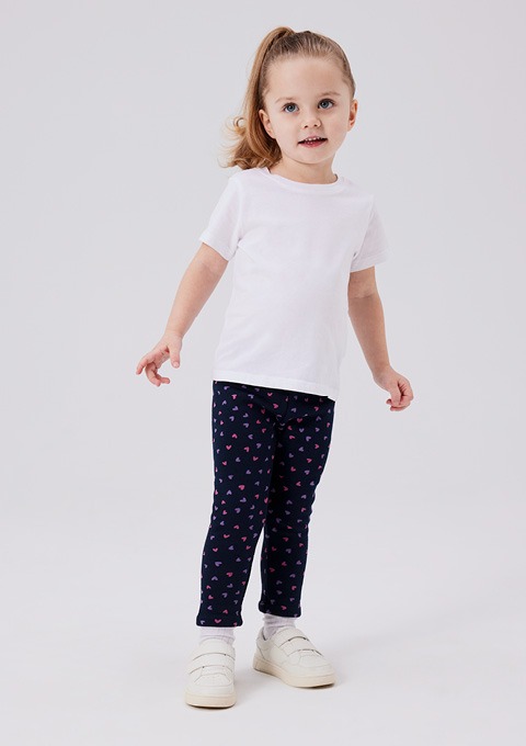 Ein kleines Mädchen trägt ein weißes T-Shirt und dunkelblaue Leggings mit Herzen. Ein kleines Mädchen trägt ein weißes T-Shirt und dunkelblaue Leggings mit Herzen.