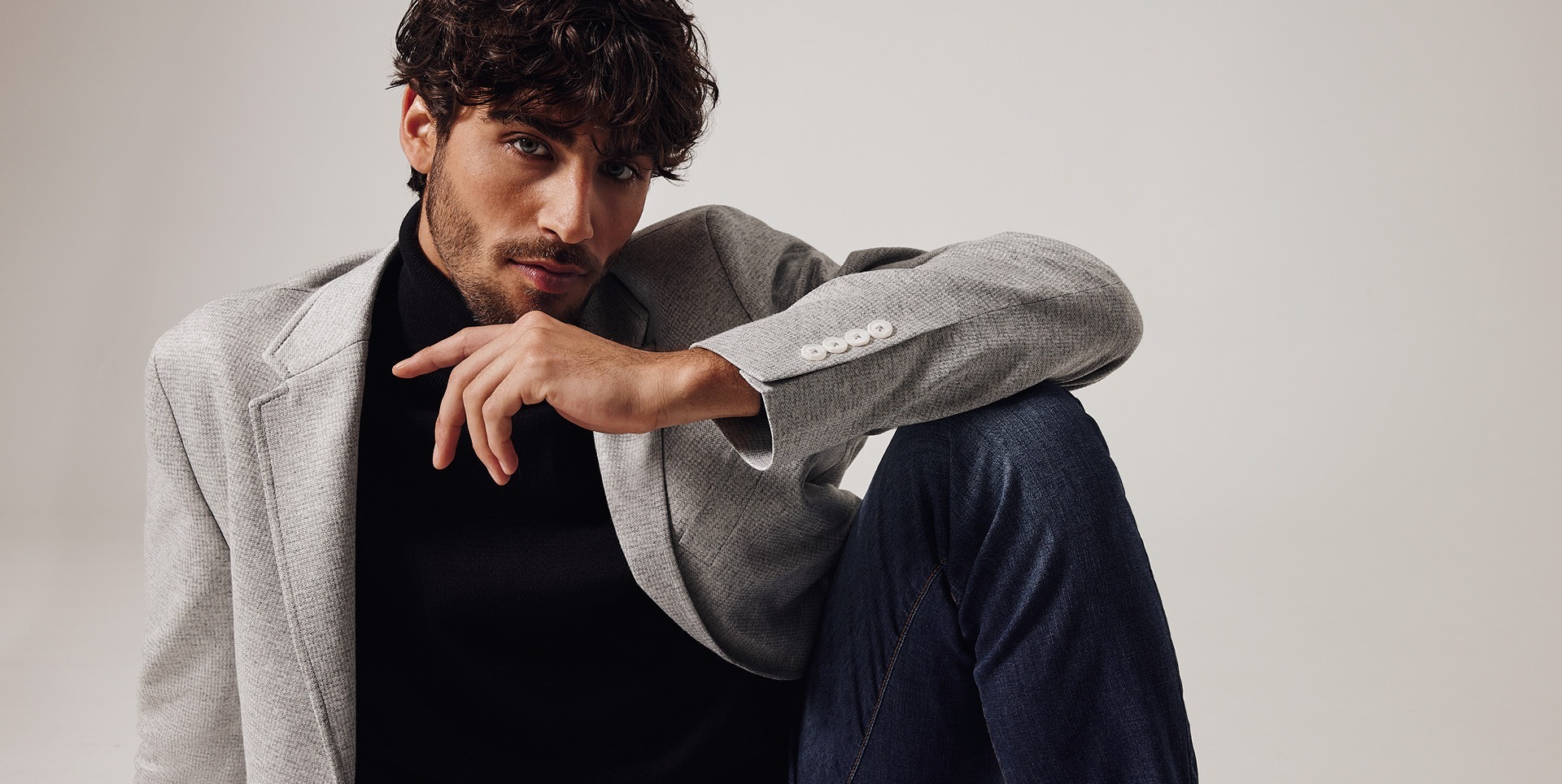 Ein junger Mann sitzt in einem grauen Blazer und schwarzem Oberteil, mit einem nachdenklichen Gesichtsausdruck. Ein junger Mann sitzt in einem grauen Blazer und schwarzem Oberteil, mit einem nachdenklichen Gesichtsausdruck.