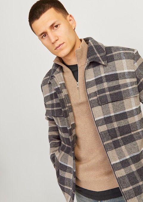 Ein Mann trägt eine karierte Jacke und einen Pullover. Er schaut in die Kamera.