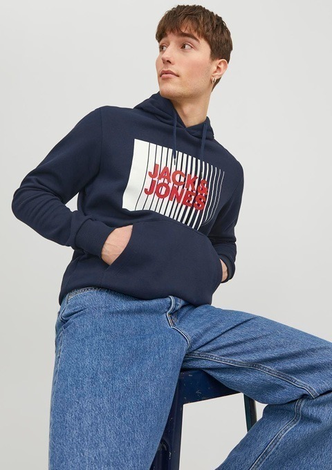 Ein junger Mann trägt einen dunkelblauen Hoodie mit dem Aufdruck "JACK & JONES" und sitzt auf einem Hocker.