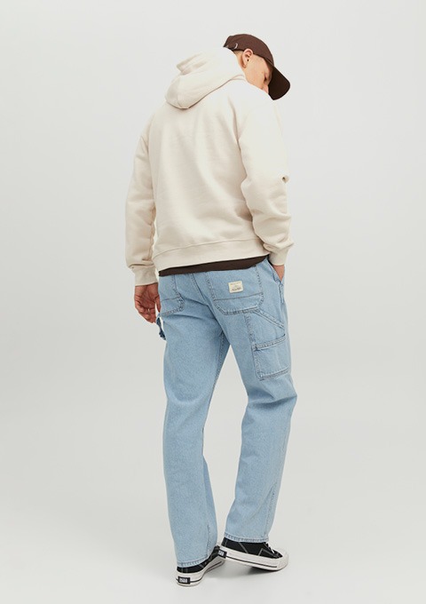Eine Person von hinten, die einen beigen Kapuzenpullover und hellblaue Jeans trägt. Eine Person von hinten, die einen beigen Kapuzenpullover und hellblaue Jeans trägt.