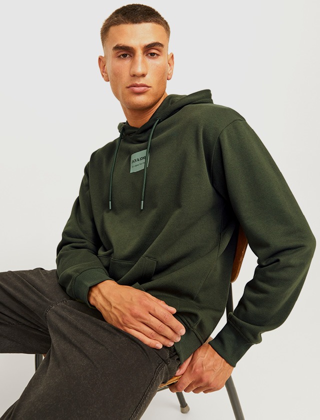 Ein Mann sitzt auf einem Stuhl und trägt einen olivgrünen Hoodie. Ein Mann sitzt auf einem Stuhl und trägt einen olivgrünen Hoodie.