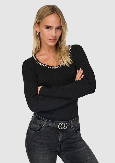 Eine Person trägt einen schwarzen, langärmeligen Pullover mit einer verzierungen am Ausschnitt und steht mit verschränkten Armen.