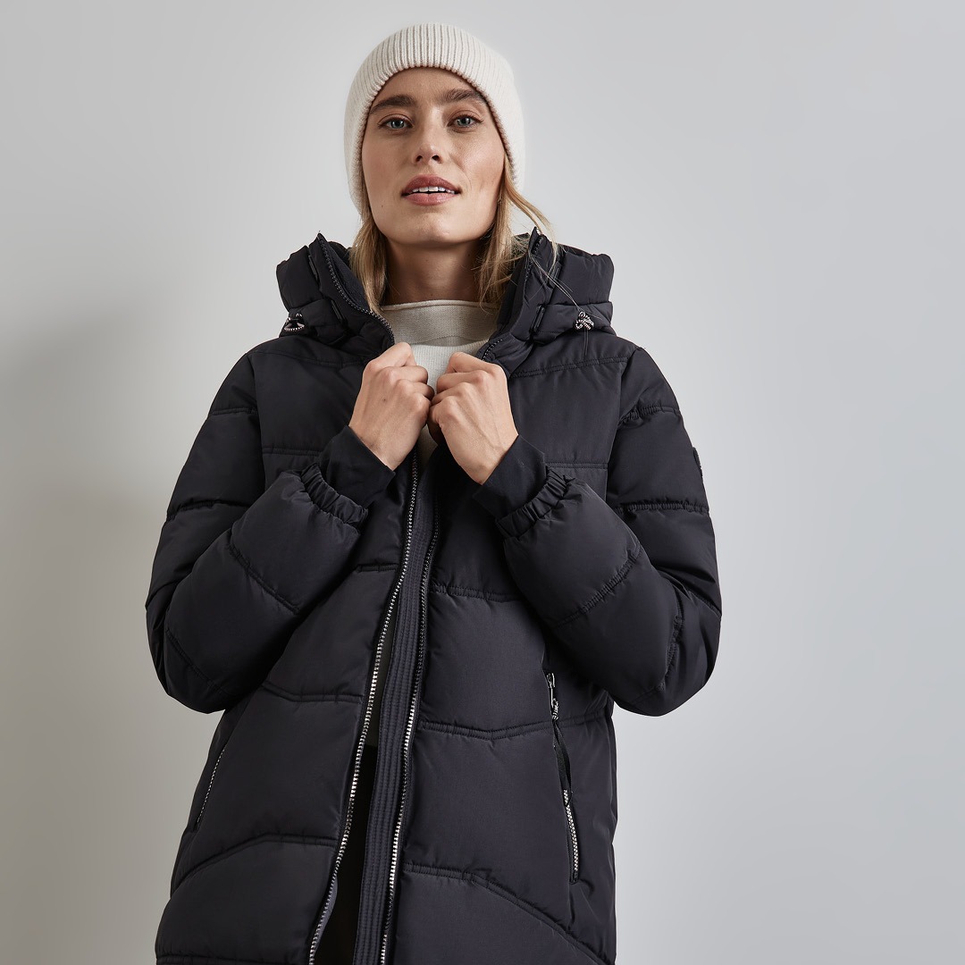 Eine Person trägt eine schwarze Steppjacke und eine helle Mütze. Eine Person trägt eine schwarze Steppjacke und eine helle Mütze.