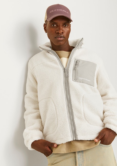 Ein junger Mann trägt eine weiße Fleecejacke mit Reißverschluss und eine lilafarbene Kappe. Ein junger Mann trägt eine weiße Fleecejacke mit Reißverschluss und eine lilafarbene Kappe.