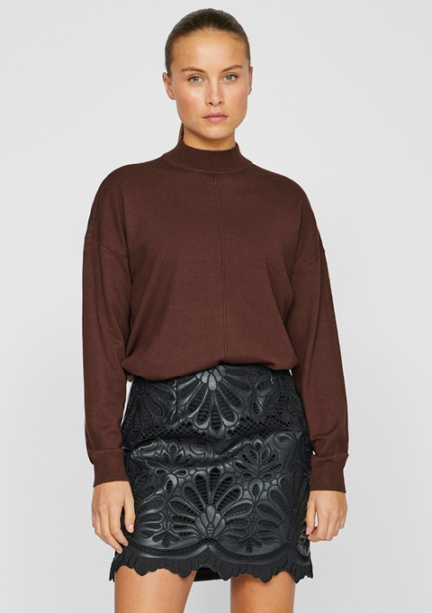 Eine Frau trägt einen braunen Pullover und einen schwarzen Rock mit Muster.
