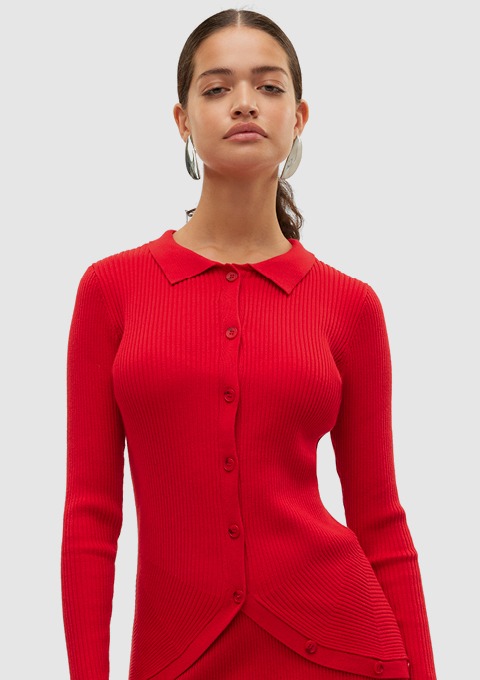 Eine Frau trägt einen roten, gerippten Pullover mit Kragen und Knöpfen.