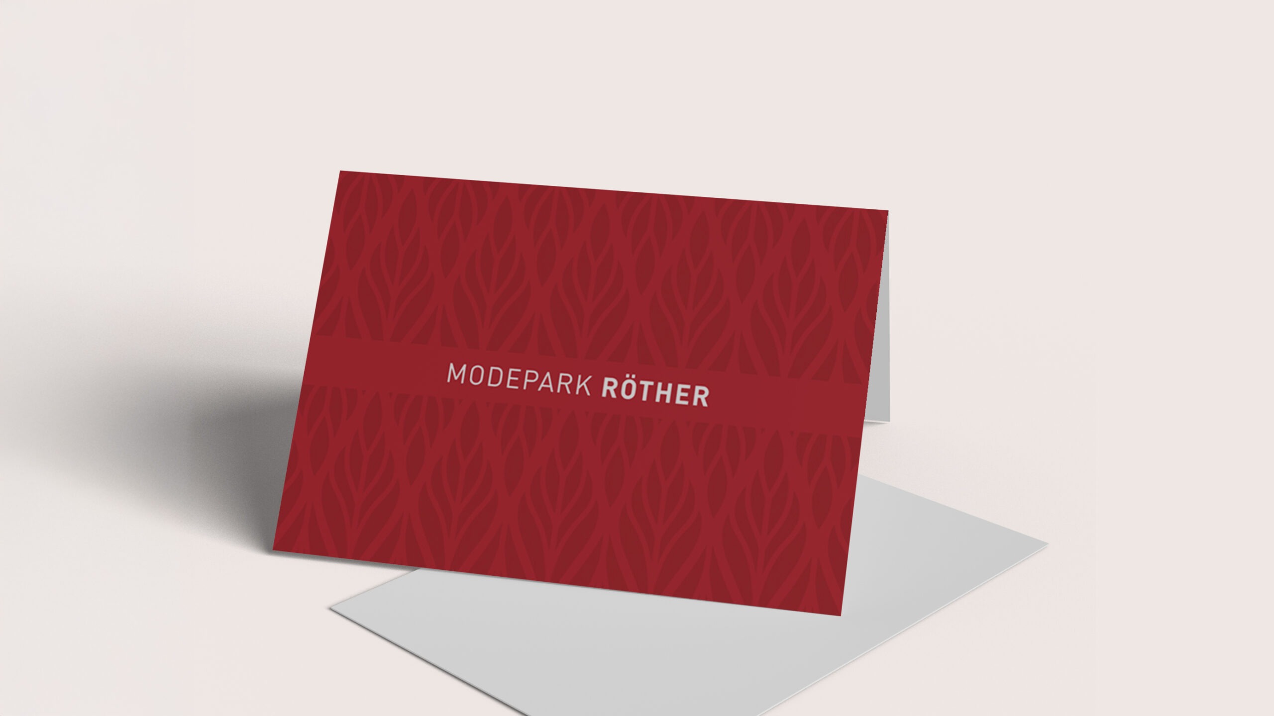Eine rote Karte mit dem Text "MODEPARK RÖTHER" und einem floralen Muster.