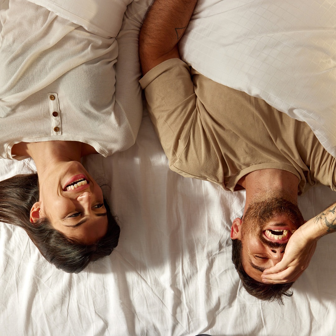 Ein lächelndes Paar liegt auf einem Bett, beide wirken glücklich und entspannt. Ein lächelndes Paar liegt auf einem Bett, beide wirken glücklich und entspannt.