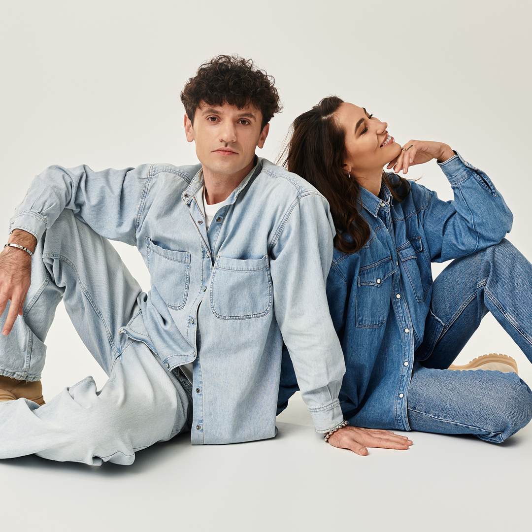 Ein Mann und eine Frau sitzen auf dem Boden, sie tragen Jeanshosen und Jeanshemden sowie beige Boots.
