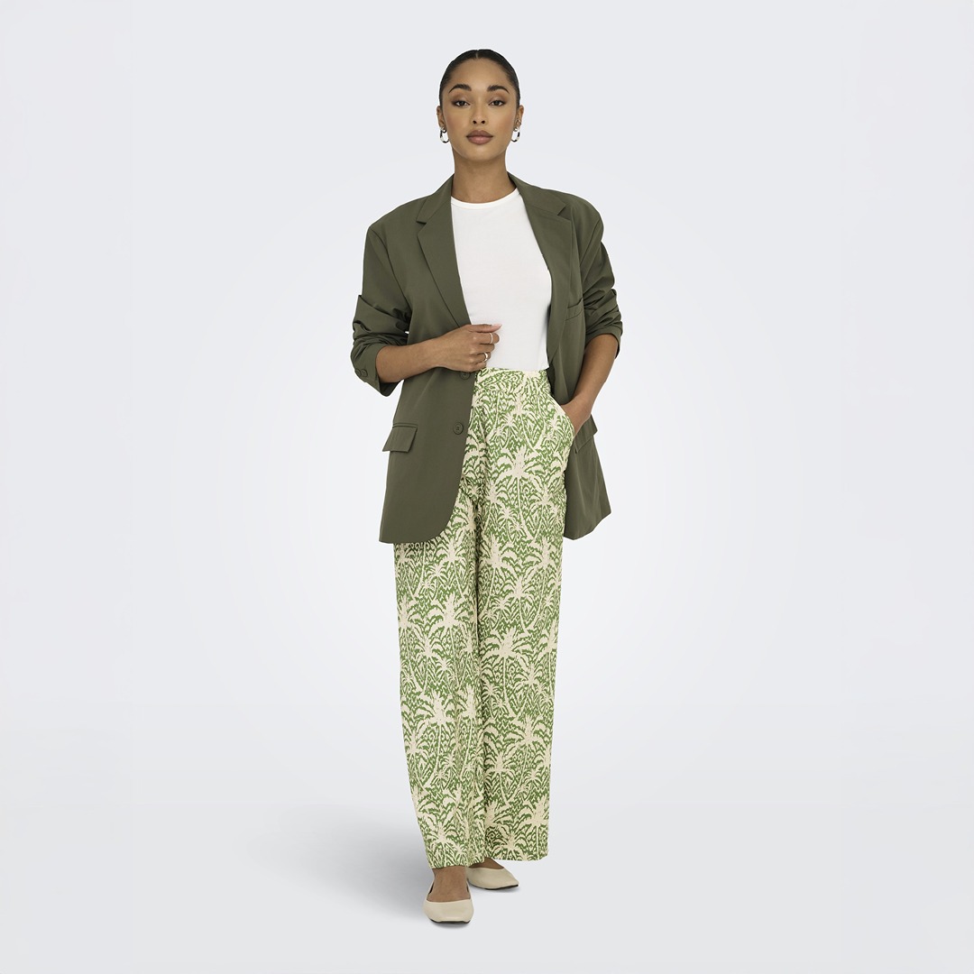 Eine Frau in einem olivgrünen Blazer und einer weißen Bluse trägt gemusterte, weite Hosen in Grün und Beige.
