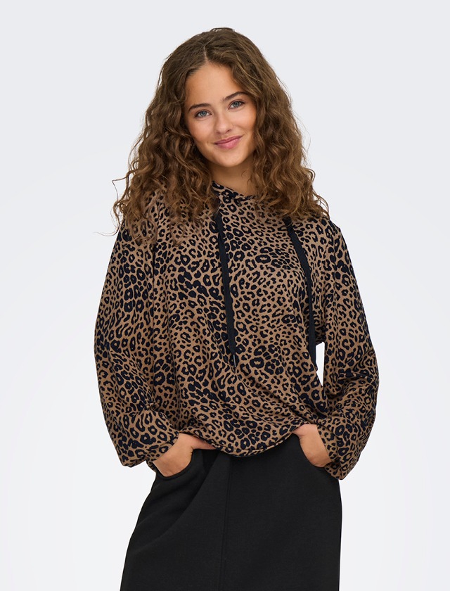 Eine Frau mit lockigem Haar trägt einen leopardenmuster Hoodie und lächelt.