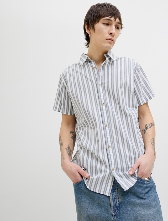 Ein Mann in einem gestreiften Shirt und Jeans posiert entspannt, mit einem freundlichen Ausdruck im Gesicht. Ein Mann in einem gestreiften Shirt und Jeans posiert entspannt, mit einem freundlichen Ausdruck im Gesicht.