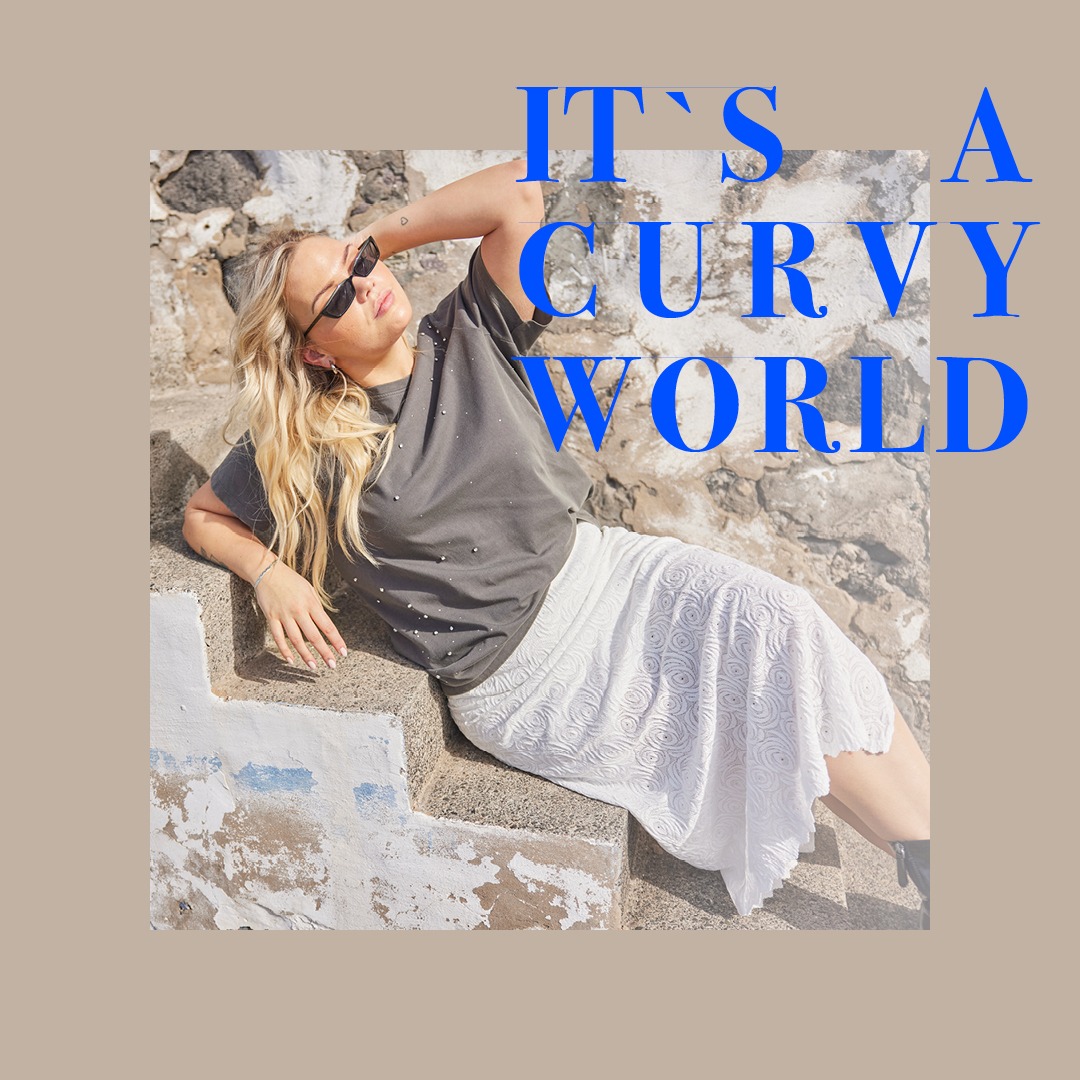 Eine Frau in einer grauen T-Shirt und einem weißen Rock sitzt entspannt auf einer Treppe mit einer Mauer im Hintergrund. In der oberen linken Ecke steht der Text "IT'S A CURVY WORLD" in blauer Schrift.